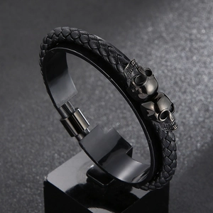 Detailed close-up of a black braided leather bracelet featuring two steel skull charms