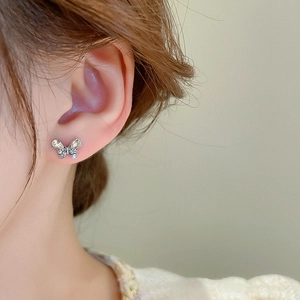 Macro detail of a silver butterfly stud earring with sparkling zircon stones on an ear lobe