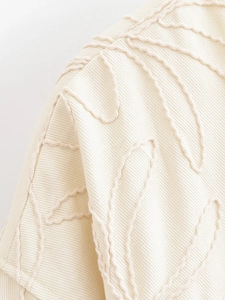 Détail de la veste crème montrant la texture du tweed et les coutures brodées ondulées