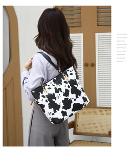 Detail view of cow print tote bag with gold metal clasp and chain on shoulder