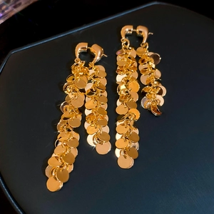 Détail de boucles d'oreilles à franges dorées avec des paillettes sur fond bleu foncé