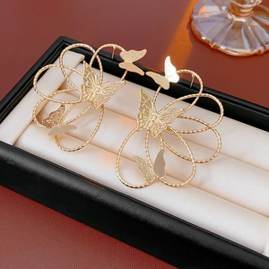 Macro shot of gold hollow butterfly earrings on a beige velvet jewelry box cushion