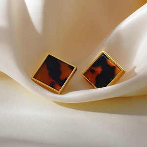 Close-up of square gold-rimmed earrings with leopard print on a silk background