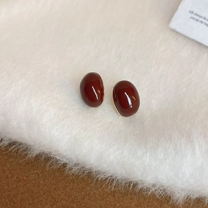 Macro view of vintage oval red-brown enamel stud earrings on white faux fur background