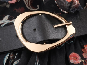 Detail of a black leather belt with an irregular gold buckle on a floral maxi dress