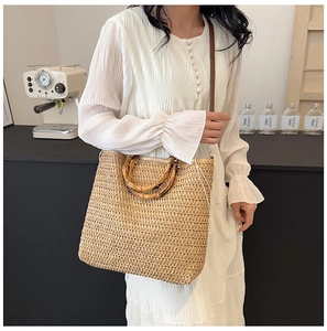 Detail of woven straw beach bag featuring a bamboo handle and long shoulder strap