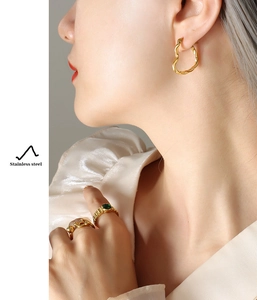 Detail of twisted gold heart earring and green gemstone ring in polished stainless steel