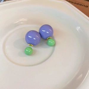 Detail of contrast color purple and green pearl stud earrings on white ceramic tray