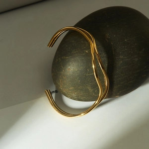 Irregular double-layer wavy gold cuff bracelet with minimalist open design on a pebble