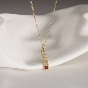 Gold necklace with LOVE pendant and red heart gemstone on white satin background