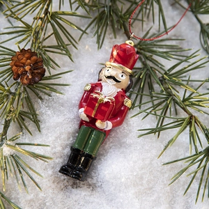 Nutcracker soldier Christmas tree ornament with gift box on festive pine branches