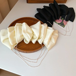 Detailed view of large satin bow hair clips with faux pearl tassels in cream and black