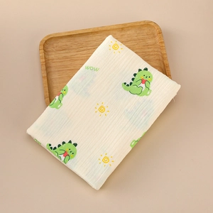 Close-up of soft double-layer muslin baby swaddle with green dinosaur and sun prints