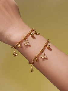 Detail van gouden roestvrijstalen armband met vlinder-, hart- en belhangers om de pols