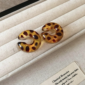 Macro shot of C-shaped leopard print resin earrings on beige velvet jewelry box