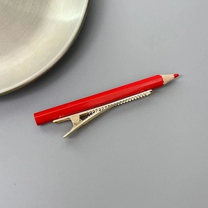 Détail d'une pince à cheveux créative en forme de crayon rouge avec base en métal doré