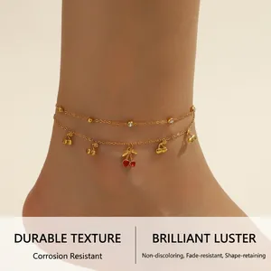 Detail of gold layered anklet with cherry pendants and rhinestones on a beach background