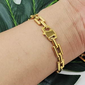Gold stainless steel square link chain bracelet set worn by a model on a green leaf background