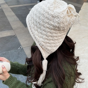 Detailed basketweave texture of cream knit earflap hat with decorative long tassels