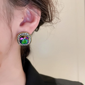 Vue macro de boucles d'oreilles carrées dorées avec pierre irisée et détails de cristaux