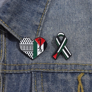 Detail of heart and ribbon enamel pins with Palestinian flag colors on denim jacket
