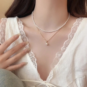 Close-up of double-layered pearl necklace with gold chain and zircon pendant on model