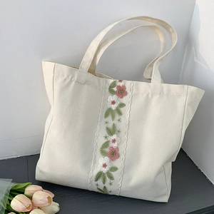 Dettaglio del ricamo floreale e del bordo in pizzo bianco su una borsa tote in tela