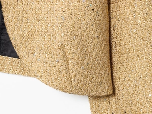 Dettaglio macro del tessuto tweed dorato con fili metallici intrecciati e paillettes