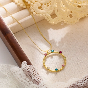 Detalle de un collar de titanio dorado con colgante redondo decorado con gemas de colores