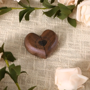 Detail of walnut heart ring box with engraved vows amidst white roses and greenery
