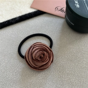 Detailed view of a brown velvet rose hair scrunchie on a textured grey background