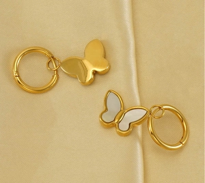 Vue détaillée de boucles d'oreilles papillon dorées avec nacre sur un tissu en satin doux