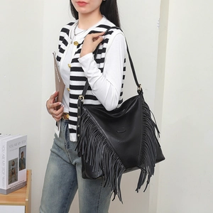 Grand sac à bandoulière noir avec rivets et détails de pompons bohèmes porté par mannequin