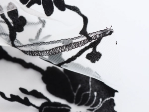 Close-up of white sheer mesh fabric with black 3D floral embroidery and lace details