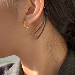 Close-up of a model wearing a gold twisted rope textured hoop earring in 925 silver