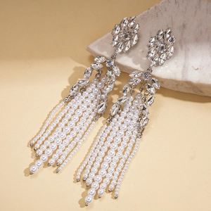 Détail de boucles d'oreilles pendantes argentées avec strass brillants et perles blanches