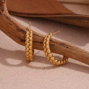 Macro detail of gold-plated hoop earrings with intricate braided texture on a branch