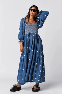 Detailaufnahme der Smok-Mieder und Gänseblümchen-Print am blauen Langarm-Kleid