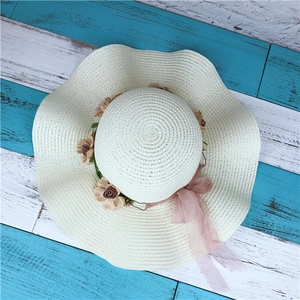 Detailed texture of woven straw sun hat with floral embellishment and pink chiffon ribbon