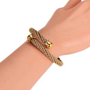 Golden woven stainless steel cable cuff bracelet with round bead tips on a hand model