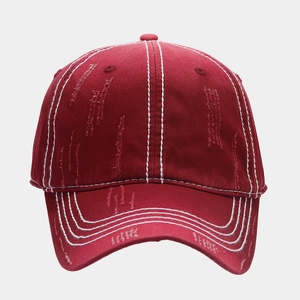 Close-up of distressed red cotton baseball cap with white contrast stitching and torn detail