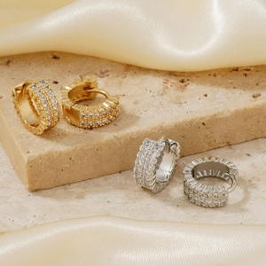 Minimalistische Creolen in Gold und Silber mit Zirkonia-Besatz auf beigem Travertin
