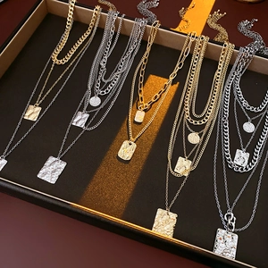 Detail of layered gold and silver necklaces with square hammered pendants on display