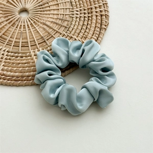 Detail of ice blue satin scrunchie showing glossy silk texture and elegant folds