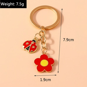 Golden keychain featuring red ladybug and flower charms on a soft pink background