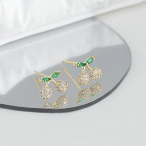 Macro detail of cherry stud earrings with green leaves and pavé white zircons on a mirror