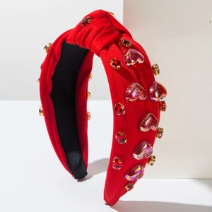 Detalle de una diadema roja anudada con brillantes pedrería de corazón en soporte blanco