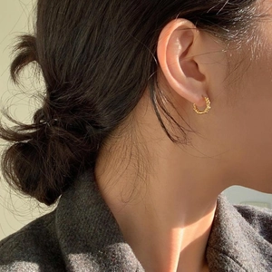 Macro shot of gold twisted rope hoop earrings worn by a model in soft natural sunlight