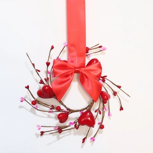 Detail of a red heart berry candle ring with dried branches and a festive red ribbon bow
