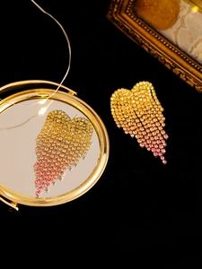 Detail of long tassel heart earrings with gradient yellow to pink rhinestones on black velvet